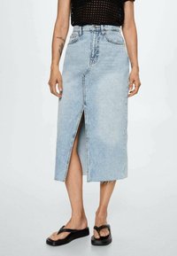 Vaaleansininen farkuhame, joka ylettyy polven alapuolelle, edessä halkio ja raaka helma. Yhdistetty mustiin flip-floppeihin rennon ilmeen saavuttamiseksi.