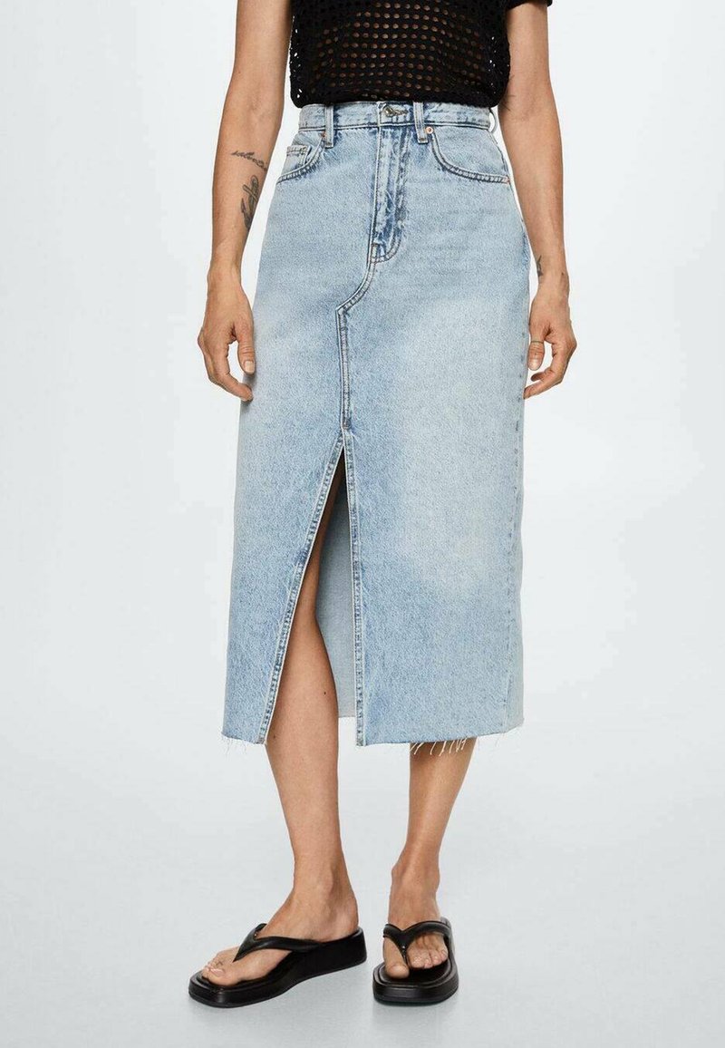 Vaaleansininen farkuhame, joka ylettyy polven alapuolelle, edessä halkio ja raaka helma. Yhdistetty mustiin flip-floppeihin rennon ilmeen saavuttamiseksi.