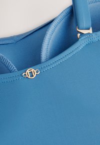 Blauer Badeanzug mit glatter, gerippter Textur. Verfügt über verstellbare Träger und ein goldfarbenes Logo-Detail auf der Vorderseite.