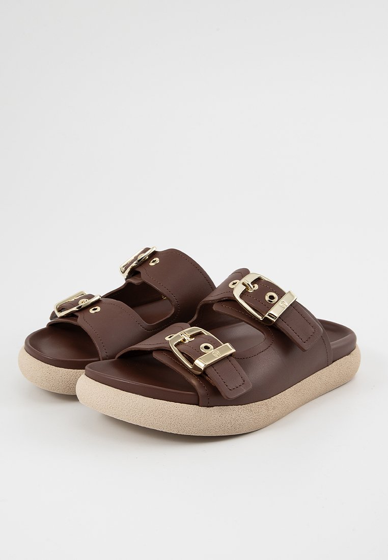 Braune Rutschsandalen aus synthetischem Material mit zwei verstellbaren goldenen Schnallen, einer gepolsterten beigen Sohle und offenem Zehenbereich.