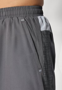 Gray athletic shorts featuring an elastic waistband, side pockets, and contrasting textured fabric panel on the side.