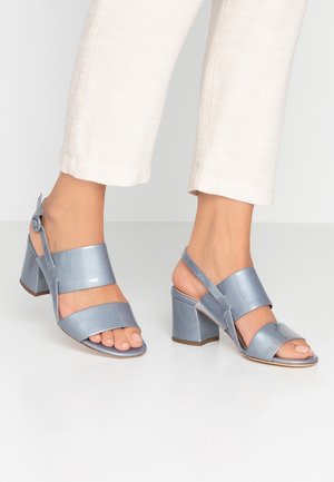 Des sandales à talons bleus présentent de larges brides mates avec un accent brillant, un bout ouvert et un talon carré. Les brides sont fixées par une boucle sur le côté.