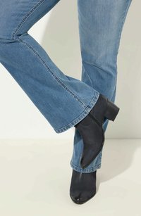 Stivaletti neri alla caviglia con punta affusolata e tacco testurizzato, abbinati a jeans svasati in denim chiaro con orlo rifinito.