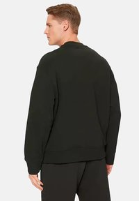 Sudadera negra con un corte relajado, mangas largas, puños y dobladillo de canalé, y diseño de cuello redondo. Textura suave sin patrones ni logotipos.