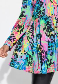 Chemise colorée à manches longues, présentant un imprimé animal dynamique en rose, bleu, vert et noir. Design évasé avec des accents de boutons.