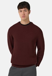 Burgundinės grioveliais megztos megztinės su apvalia apykakle ir nuleistomis pečių linijomis, su tekstūruotu raštu ir laisvu siluetu ties liemeniu.