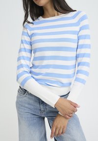 Pull en maille rayé bleu clair et blanc avec un col arrondi et des poignets côtelés, assorti à un jean en denim clair.