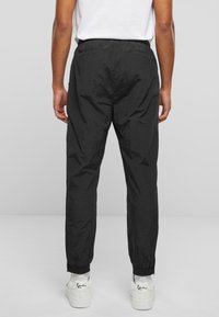 Pantaloni de vânt negri, ușori, cu talie elastică și manșete, asortați cu adidași albi. Textură netedă, fără modele.