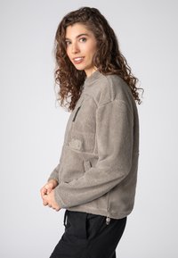 Grau melierter Fleecepullover mit hohem Kragen, Reißverschlusstasche auf der Brust und Seitentaschen. Weiche Textur und lockere Passform, mit verstellbarem Saum.