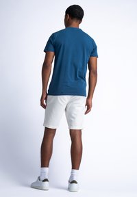Teal t-shirt met korte mouwen, van katoen, effen kleur, gecombineerd met lichtbeige shorts, witte sokken en lichte sneakers, gezien vanaf de achterkant.