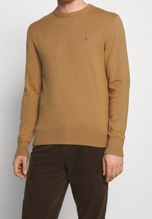 Pull en maille jaune moutarde avec col rond et manches côtelées. Détail de petit logo sur la poitrine. Texture douce et design ajusté.