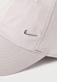 Ανοιχτό γκρι καπέλο από απαλό ύφασμα, με κυρτή γείσο, λεπτομερείς ραφές και ασημί λογότυπο Nike στο μπροστινό μέρος.