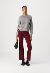 Suéter gris de punto, pantalones de pana burdeos de pierna acampanada, bolso negro y zapatos chunky negros. Textura suave, corte relajado y escote redondo.