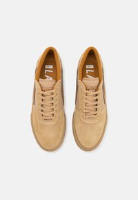 Tan suede sneakers with beige laces and a brown side stripe, featuring a padded collar and textured rubber sole. Interior has orange accents.