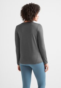 Long-sleeve gray top made of soft material, with a curved hem and wrist cuffs, paired with light blue athletic leggings.