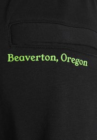 Svart tyg har texten "Beaverton, Oregon" i klargrön broderi, placerad på fickområdet med en slät yta.