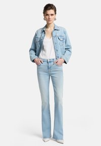 Giacca di denim azzurro chiaro con tasche frontali, abbinata a jeans a zampa d'elefante azzurri chiari con una texture sfumata e vita alta. T-shirt bianca sotto.