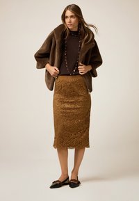 Brun fuskpälsjacka, mörkbrun topp, figursydd bronzfärgad spetskjol och svarta spetsiga ballerinas med rosett. En lång pärlnekedj bärs.