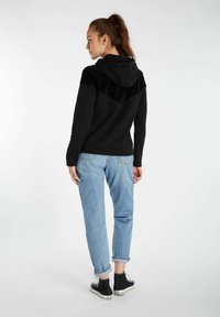 Zwarte hoodie met een gestructureerde bovenkant, gecombineerd met lichtblauwe jeans met opgerolde manchetten en zwarte sneakers. Eenvoudig ontwerp, losse pasvorm.