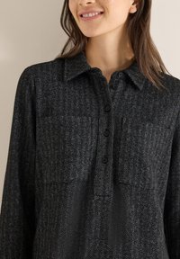 Camisa de patrón espiga en negro y gris, con cuello, tapeta con botones y dos bolsillos en el pecho. Tejido suave con acabado texturizado.