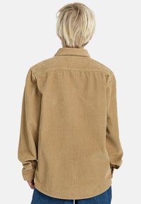Kordurová košeľa v pieskovej farbe, s stredne ťažkým textúrovaním, golierom na gombíky a dlhými rukávmi. Zadný pohľad zobrazuje rebrovaný vzor a uvoľnený strih.
