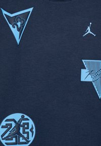T-shirt blu navy con grafiche azzurro chiaro, tra cui una silhouette del Jumpman, motivi triangolari e un logo circolare con "23".