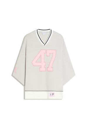 Light beige oversized V-neck shirt with wide sleeves, large pink number 47 on front, black trim on collar and hem, and small label at bottom.