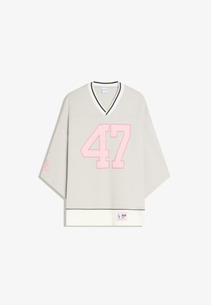 Light beige oversized V-neck shirt with wide sleeves, large pink number 47 on front, black trim on collar and hem, and small label at bottom.