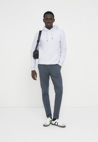 Ανοιχτό γκρι φούτερ με κουκούλα και τσέπη καγκουρό, σκουρό μπλε στενά παντελόνια και μαύρη τσάντα χιαστί. Λευκά αθλητικά παπούτσια με μαύρες ρίγες.