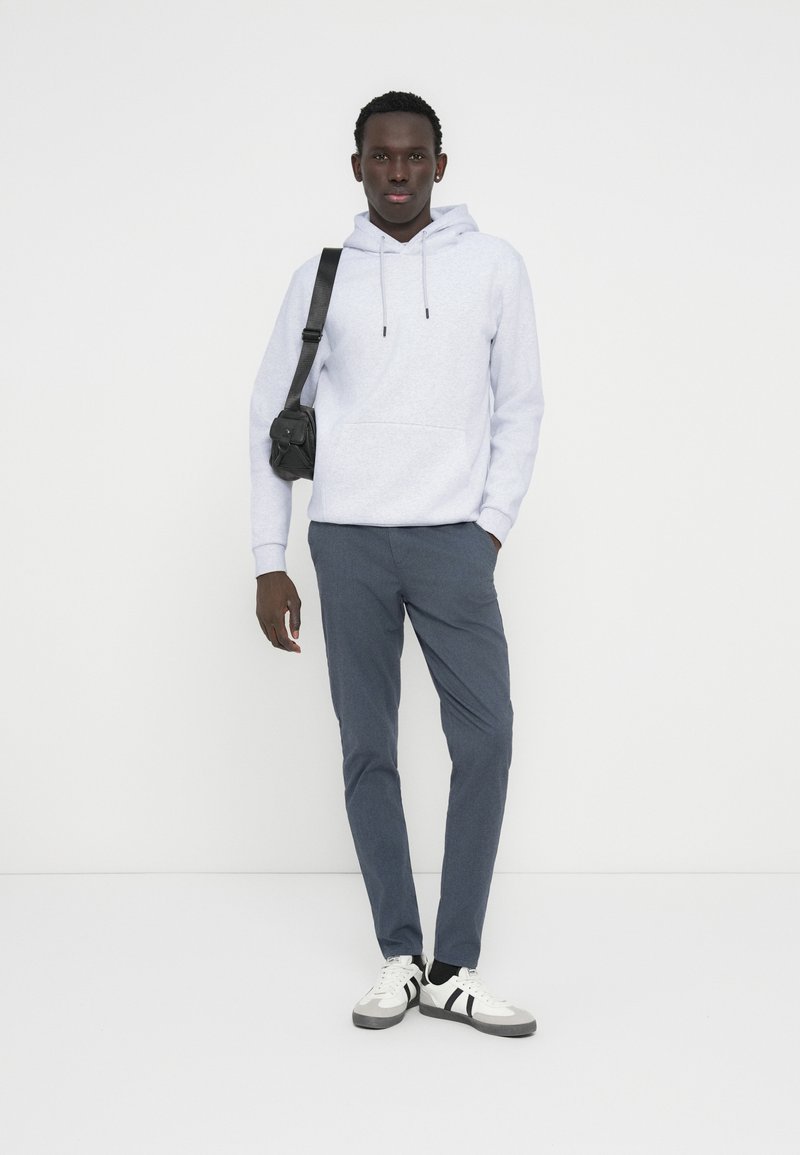 Ανοιχτό γκρι φούτερ με κουκούλα και τσέπη καγκουρό, σκουρό μπλε στενά παντελόνια και μαύρη τσάντα χιαστί. Λευκά αθλητικά παπούτσια με μαύρες ρίγες.