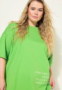 T-shirt de gran tamaño en un verde brillante, fabricada en suave algodón, con mangas cortas y un detalle de texto en blanco impreso en la parte frontal.