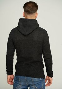 Sweat à capuche noir en maille avec une finition texturée, doté d'une capuche et de manches longues. Le design comprend une silhouette ajustée avec un ourlet côtelé.