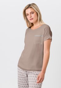 Beige T-shirt met korte mouwen, ronde hals en een voorkantzak met een zilveren gestreepte accent. Zachte textuur, casual pasvorm. Gekleurde broek eronder.