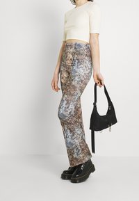 Oblékané, vysoké kalhoty s mnohobarevným potiskem hada, spárované s krémovým nitěným crop topem a černými platformovými botami. Nese malou černou tašku.