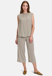 Lätt, mönstrad tvådelad outfit bestående av en ärmlös topp och capribyxor i beige med geometriska mönster. Bruna slip-on skor.