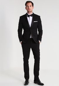 Tuxedo nero con rever in satin, camicia bianca e papillon nero. Design slim-fit con pantaloni a gamba dritta e scarpe nere lucide.