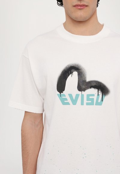 Balta medvilninė marškinėliai su juodu purškiamu dizainu virš žodžio "EVISU" šviesiai mėlynos spalvos, su šviesiai mėlynomis purslų detalėmis šalia apatinės dalies.
