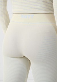 Leggings beige acanalados con rayas azul claro, de diseño ajustado y cintura con marca. La tela parece suave y elástica.