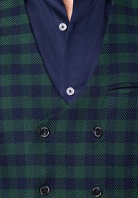 Dwurzędowa marynarka w zielono-granatową kratę, z dekoltem w serek, dużymi czarnymi guzikami i granatową koszulą pod spodem.