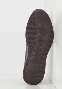 Suola di scarpa in gomma marrone con superficie testurizzata, caratterizzata da un motivo a onda e scanalature di presa pronunciate. Include un marchio vicino al tallone.