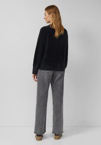 Ciemnoszary sweter z dzianiny o luźnym kroju, w zestawieniu z wysokimi, szerokimi szarymi dżinsami i beżowymi botkami za kostkę. Widoczna jest miękka faktura.