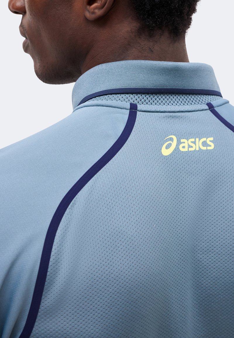 Mann trägt ein hellblaues Sportshirt mit dunkelblauen Nähten und gelbem ASICS-Logo im oberen Rückenbereich.