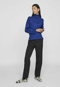 Zils džemperis ar augstu apkakli un ribojumiem pie piedurknēm un apakšējās malas, apvienots ar melniem biksēm. Apavi ar melnbaltu rakstu.