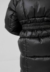 Sort pufferjakke med quiltet design, elastisk talje og glansfuld finish. Materialet ser glat og vandafvisende ud.