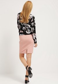 Sort blomsterprintet sweater med lange ærmer, der er parret med en lyserød tætsiddende nederdel med en slids bagtil og sorte ankelremssandaler.