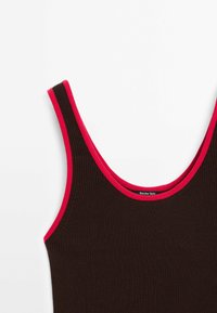 Bruine geribde tanktop met brede schouderbanden, voorzien van een contrasterende felrode afwerking langs de halslijn en armsgaten. Merkenlabel zichtbaar.