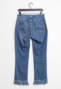 Džínové kalhoty v středně modré barvě s ošoupaným lemem, s vysokým pasem, pěti kapsami a hladkým povrchem. Visí na  černém plastovém háčku.