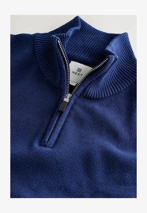 Marineblauwe gebreide zip-up trui met een staande ribbelkraag en zilveren ritsdetails. Heeft een zachte textuur en een merklabel aan de binnenkant.