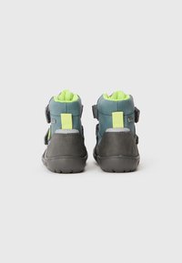 Zwei knöchelhohe Schuhe mit einem tealfarbenen Obermaterial und grauen Akzenten, Klettverschlüssen und einem leuchtend grünen Futter. Strukturierten Gummisohlen.