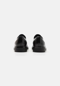Chaussures en cuir noir avec une finition lisse, bout rond et semelles basses, présentant des coutures latérales et un design minimaliste.